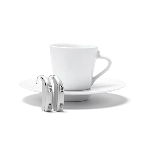 Behind The Ear two behind the ear (BTE) hearing aids standing on end in front of a coffee cup on a saucer