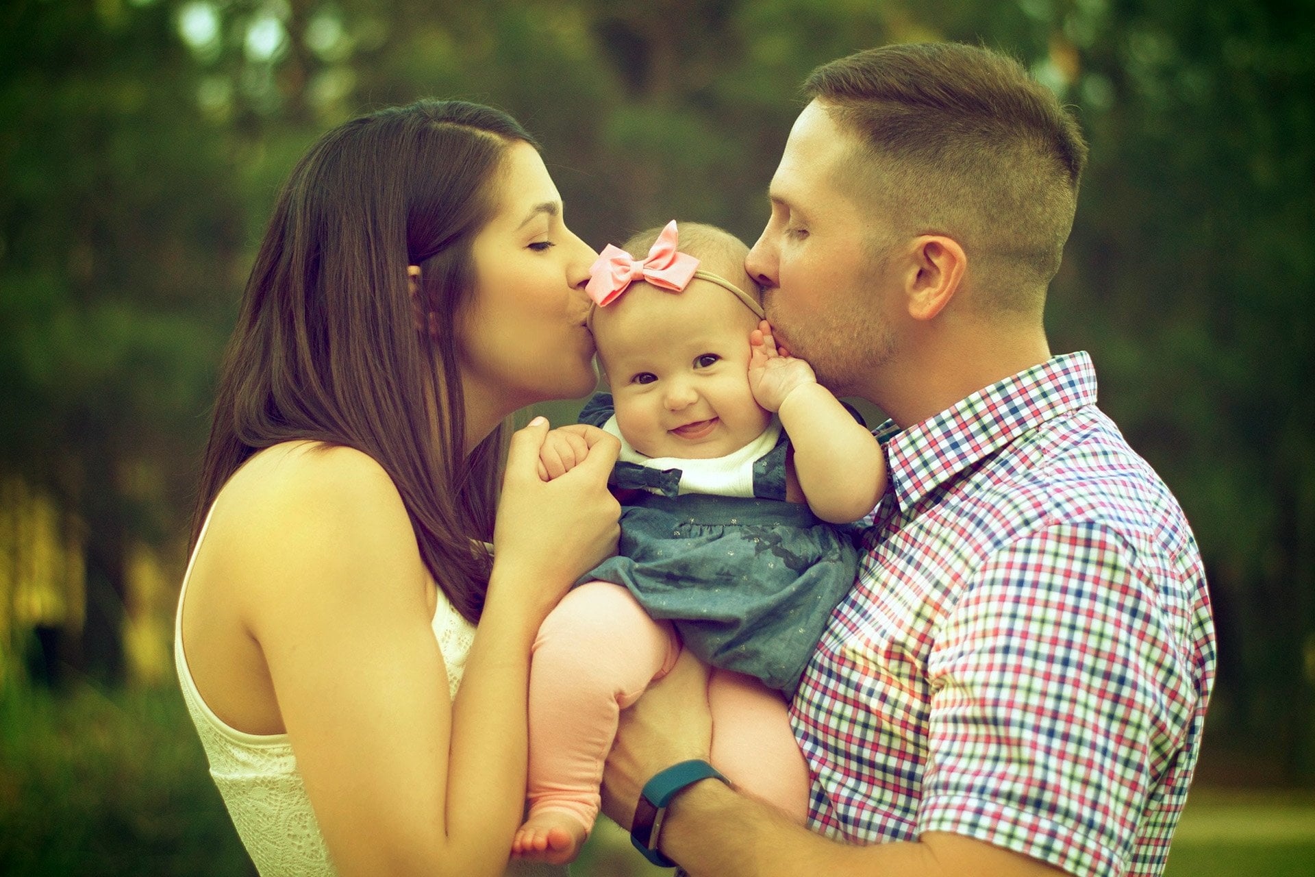 parents kissing toddler in the woods