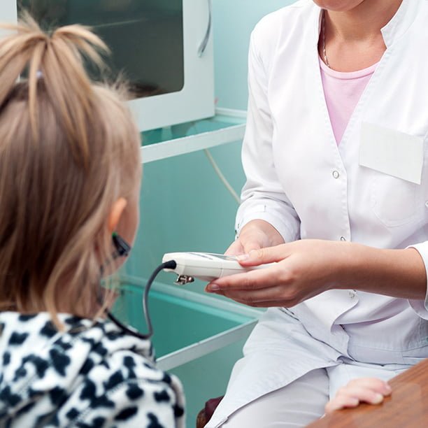 Female doctor holding a hearing instrument testing a little girls ear