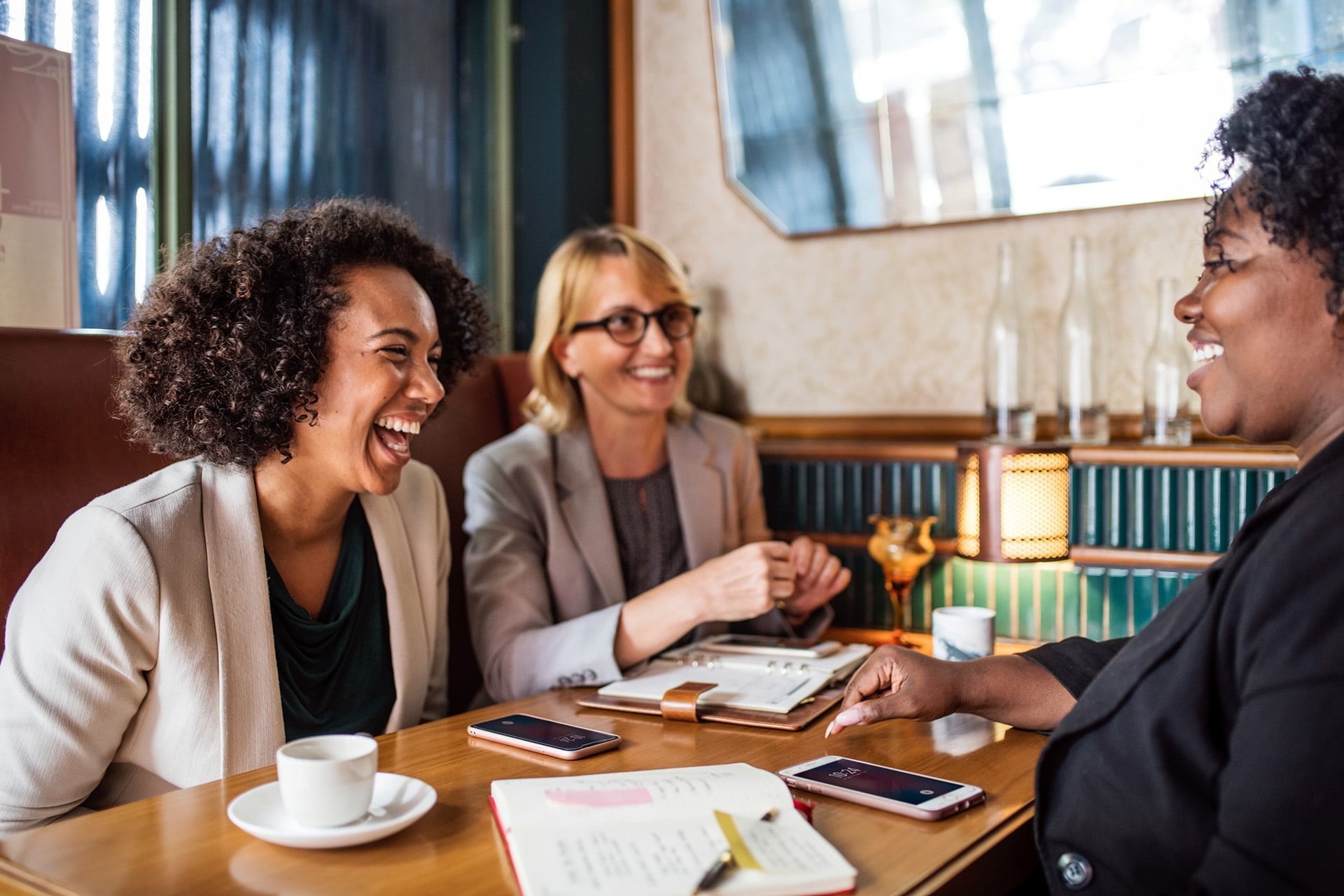 three women sitting at a restaurant table conversing and laughing