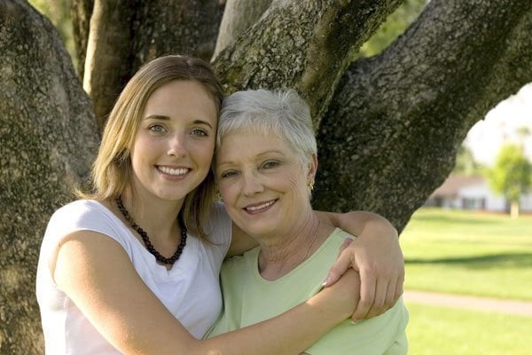 Daughter holding mother standing in front of a tree smiling