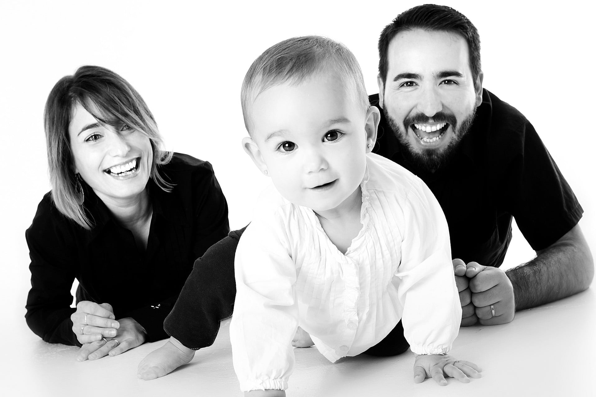 black and white image of family laying on the floor smiling with the parents behind the infant