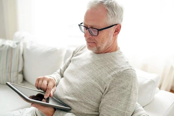elderly man sitting on a couch reading and navigating a tablet