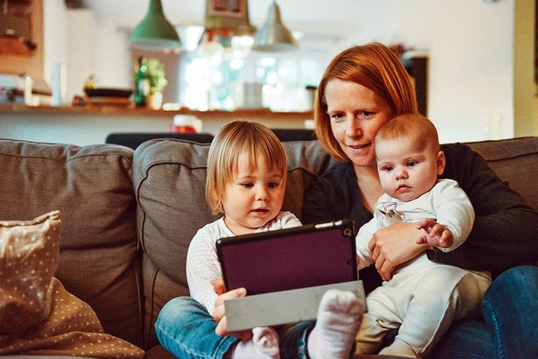Mother with two young children sitting on a couch looking at a tablet
